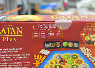 The packaging of the game 'Catan Plus' featuring awards and information about game content and expansions.