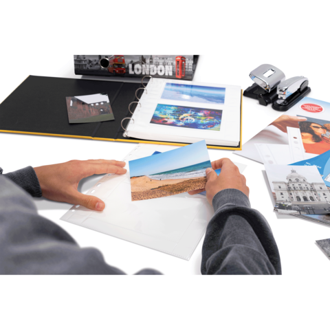 Eine Person hält ein Foto von einem Strand in der Hand, während sie ein Fotoalbum und verschiedene Dokumente auf einem Tisch betrachtet.