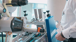 A person is operating a modern labelling machine equipped with various tools and a blue control panel.
