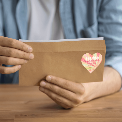 Eine Person hält einen braunen Umschlag mit einem Herzaufkleber, auf dem "Save the Date" steht.