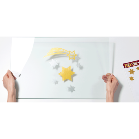 Hände halten eine transparente Folie über bunten Sternen und Dekorationselementen in verschiedenen Farben.