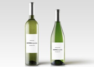 Two bottles of white wine with labels: one Chardonnay from 2016 and one Riesling from 2017, both named 'HERMAexquisite.