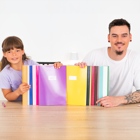 Ein Kind und ein Erwachsener sitzen an einem Tisch und halten bunte Ordner. Der Erwachsene lächelt, während das Kind neugierig schaut.