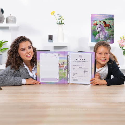 Two girls are sitting at a table, holding an open notebook with a certificate and a blank sheet of paper. Decorative elements are visible in the background.