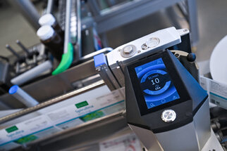 A digital control panel with a blue display and buttons, which is part of an industrial machine for processing or packaging.