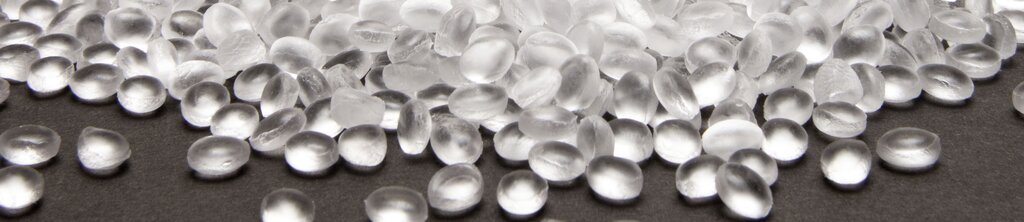 Transparent, round pearls rest on a dark surface that has a smooth and shiny texture.