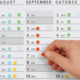 Ein Hand, die einen roten Punkt auf einem Kalenderblatt für September und Oktober anzeigt, mit Daten und Wochentagen.
