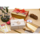 Geschenkpäckchen in gold und weiß mit Punkten, umgeben von Dekorationen wie Kerzen, einer Tannenzapfen und Geschenkband.