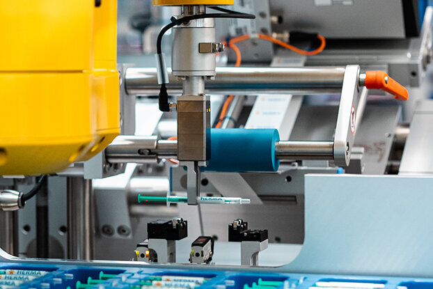 Industrial robot with a yellow arm working at a manufacturing station to assemble electronic components.