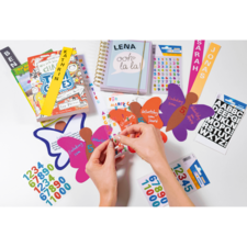 Hände, die bunte Aufkleber auf Schmetterlingsformen anbringen, umgeben von Schulmaterialien wie Notizbüchern und Aufklebern.