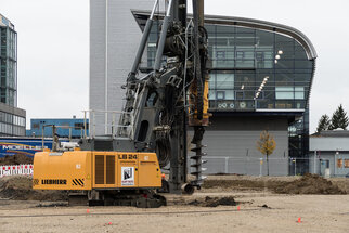Construction equipment of the type Liebherr LB 24 at a construction site, surrounded by modern buildings. The drill is embedded in the ground.