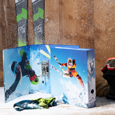 Ein Skimappe mit Bildern von Skifahrern in Aktion, umgeben von Skiausrüstung und Schnee. Skier stehen im Hintergrund.