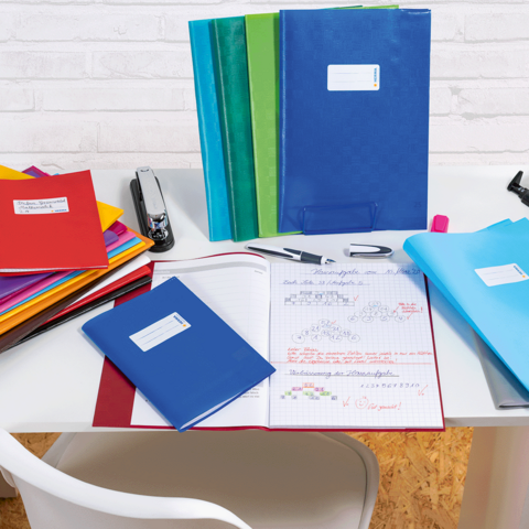 Eine Frau und ein kleines Mädchen sitzen an einem Tisch und blättern durch ein Heft. Bunte Stifte und Materialien liegen auf dem Tisch.