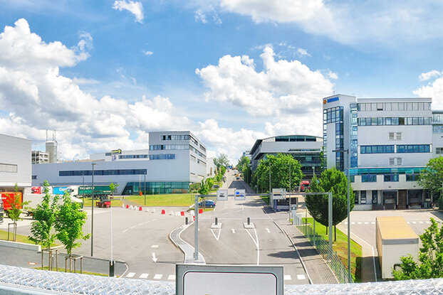 Panoramic view of a modern industrial building with adjacent office buildings and a clear blue sky.