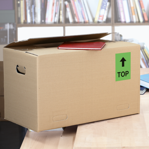 Ein Karton mit dem Aufkleber "FRAGILE", daneben ein graues Kuvert mit dem Aufkleber "URGENT!" und eine Schere.