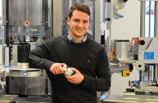 A man is holding a glass and standing next to a modern filling machine in a production environment.