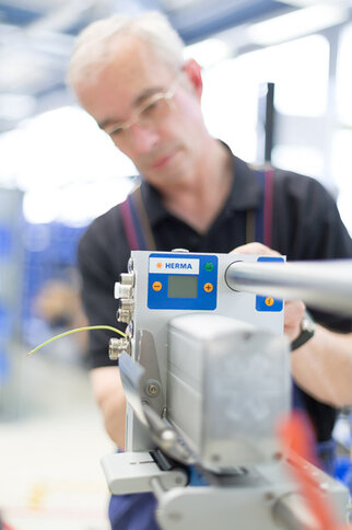 A man is operating a device from HERMA that is used for labelling. The focus is on the control panel of the device.