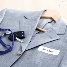 Grau blazer mit einem Namensschild "Mr. Miller", einem Schlüsselbund und einem Schlüsselanhänger auf einem Holzständer.