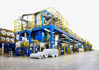A modern production facility with blue and yellow machines that process paper rolls and materials.