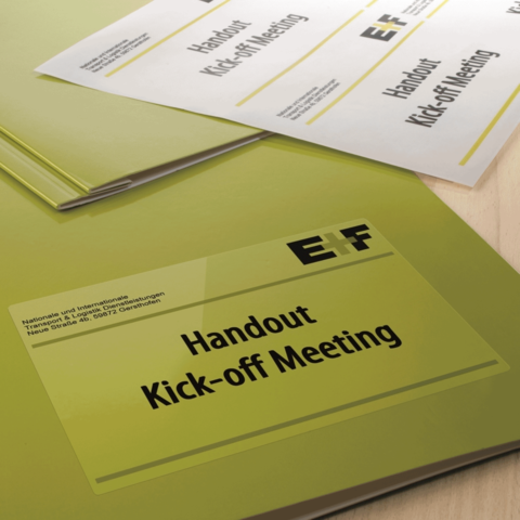 Handouts für ein Kick-off-Meeting in grünen Ordnern, mit dem Titel "Handout Kick-off Meeting" auf einem Tisch.