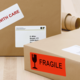 Paket mit einem Aufkleber "Vorsicht" und einem anderen Aufkleber "Zerbrechlich", adressiert an D. Miller in Stuttgart.