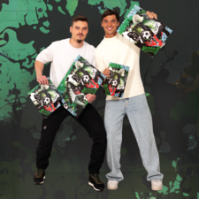 Zwei Männer posieren mit Kunstdrucken, die einen Fußball und Tiere zeigen, vor einem bunten, grafischen Hintergrund.