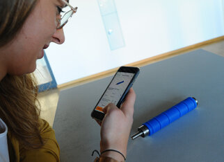 A person with glasses is looking at their smartphone while a blue pen lies on the table.