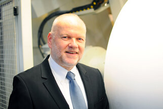 A man in a suit stands next to a large, round machine in a technical setting.