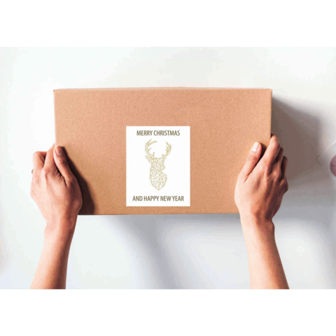 Geschenkbox in den Händen mit einem Etikett, das "Frohe Weihnachten und ein glückliches neues Jahr" zeigt, dekoriert mit einem Rentiermotiv.