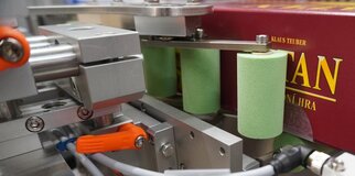 Machine parts with green cylinders and a red packaging in the background, used for an automated production process.