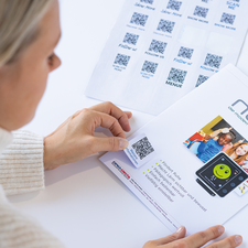 Eine Person scannt einen QR-Code auf einem Menblatt, whrend ein weiteres Blatt mit mehreren QR-Codes im Hintergrund liegt.