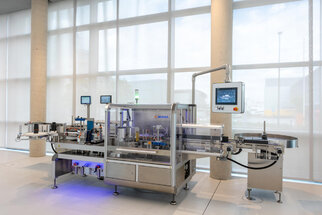 A modern packaging machine with multiple stations, screens, and a transparent casing in a bright room.