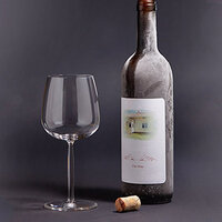 A bottle of wine with a label and a glass beside it, set against a dark background. A cork lies on the ground.