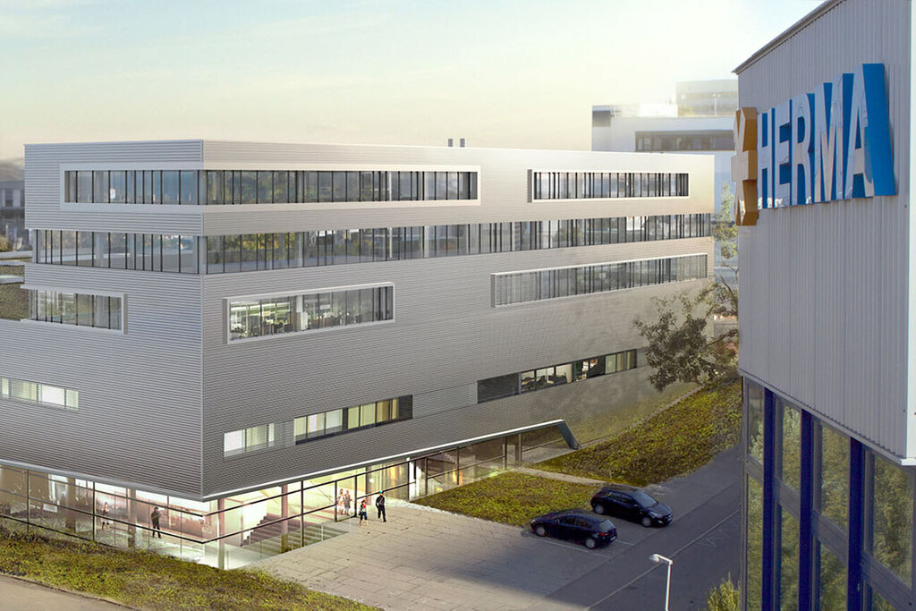 Modern office buildings with flat rooftops and large windows, surrounded by green space and a parking lot.