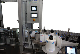 Automatic labelling machine with multiple rolls, control unit, and labels on bottles.