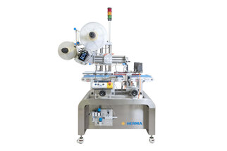 Automatic labelling machine with multiple rolls, equipped with sensors and control elements, on a sturdy table.