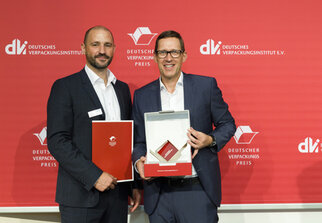 Two men stand side by side, holding awards in their hands. In the background, there is a red banner featuring the logo of the German Packaging Institute.