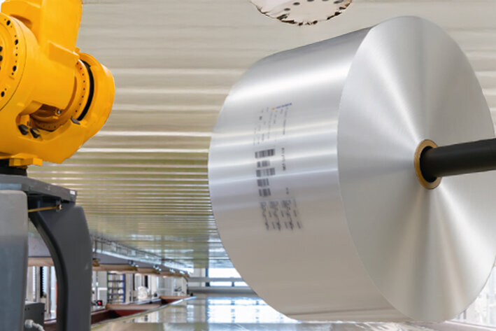 A yellow industrial robot arm is assembling a large, silver component in a modern manufacturing environment.