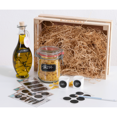 Ein Holzbehälter mit Heu, gefüllt mit einer Flasche Olivenöl, einem Glas Pasta, Etiketten und Aufklebern.