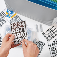 Hands hold a card with black numbers on a white background, surrounded by various stickers and an organizer.