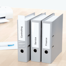 Drei graue Ordner mit den Beschriftungen "Controlling", "Service" und "Finance" stehen auf einem Tisch.