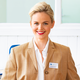 A smiling woman with blonde hair is wearing a beige blazer and a white blouse. A name tag reads 'Manuela Richter'.