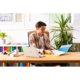 Ein junger Mann sitzt an einem Schreibtisch, arbeitet mit einem Laptop und blättert durch Dokumente in einer Ordnermappe. Pflanzen sind im Hintergrund.