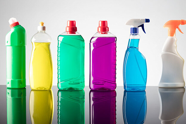 Row of cleaning product bottles in various colours on a reflective surface.