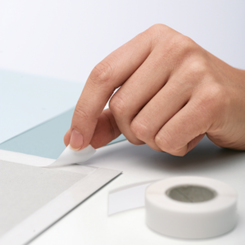 A hand removes a piece of tape from a gray surface, while another piece of tape lies beside it.