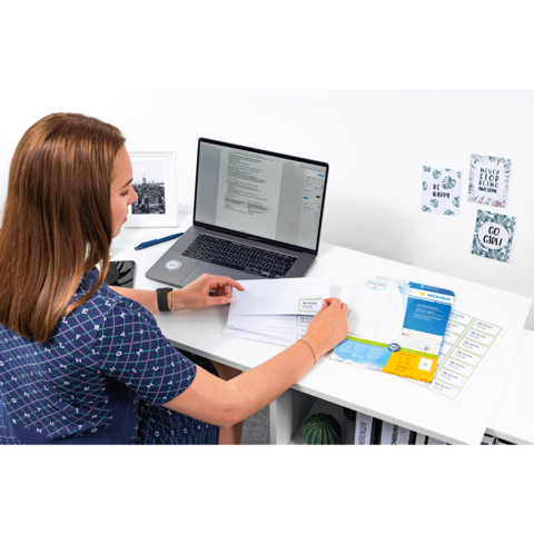 Eine Frau sitzt an einem Schreibtisch, arbeitet am Laptop und sortiert Dokumente sowie Briefe.