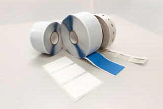 Two rolls of label material, one with a blue surface and one with a white surface, along with several blank labels on a table.