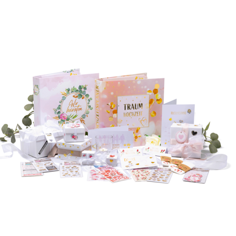 Hochzeitsplanungsset mit zwei Fotoalben, Geschenken, Aufklebern und Dekorationen in Pastellfarben, umgeben von Eukalyptusblättern.