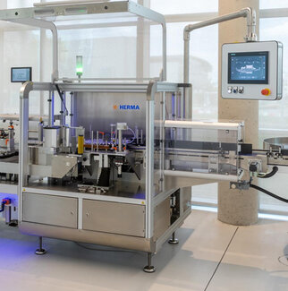 Automated labelling machine from HERMA with a control panel and various mechanical components for labelling products.