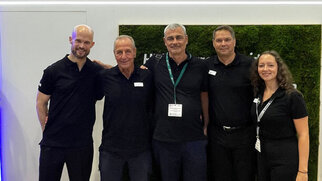 Five people in black clothing stand side by side in front of a wall featuring the HERMA logo and the slogan 'Coating your success.